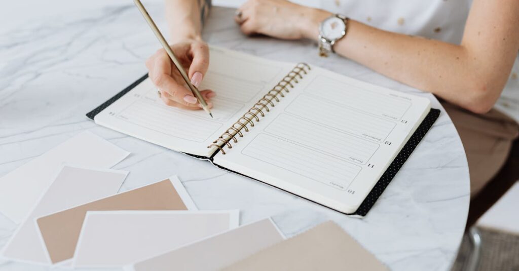 A woman writes in a planner on a marble table, surrounded by swatches. Creative and organized workspace.